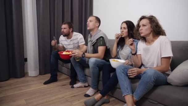 Caucasian company of young friends watch the match on TV with interest, experience and express their emotions brightly, noting the victory of their favorite team. They shout, raise their hands, stand - Πλάνα, βίντεο