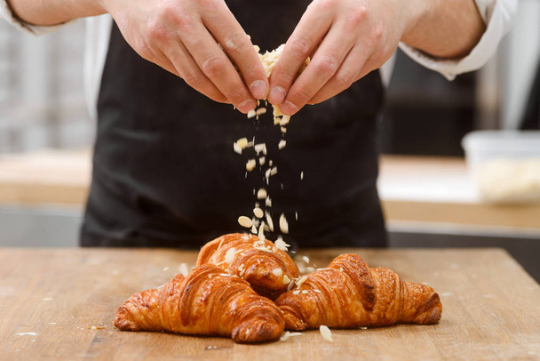 Baker sprinkles croissants with almond - Фото, изображение