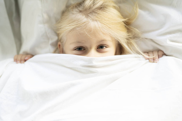 A little girl in bed below the covers - 写真・画像