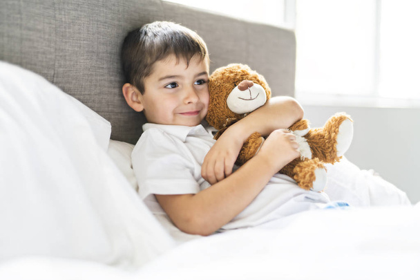 A Child lying in bed with a plush teddy bear - Фото, изображение