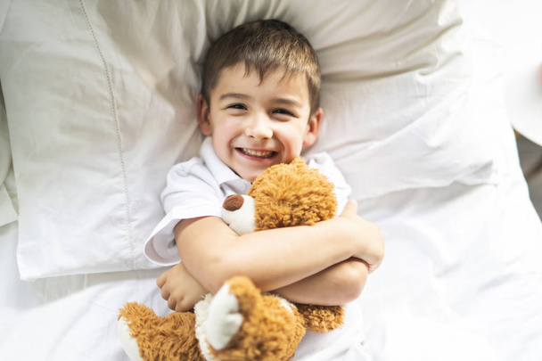 A Child lying in bed with a plush teddy bear - 写真・画像