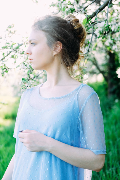 Nyugodt, szép fiatal nő a kertben, átlátszó kék ruhát visel - Fotó, kép