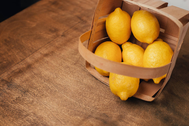 Yellow colorful lemons in the basket in the right side of the bright wooden table horizontal - 写真・画像