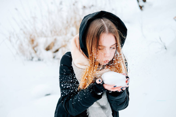 Atrakcyjny blond młoda kobieta dorosłych zabawy z pierwszym śniegiem sobie dorywczo strój czarna parka, dżinsy, różowy skórzane buty i plecak i beżowy szal - Zdjęcie, obraz