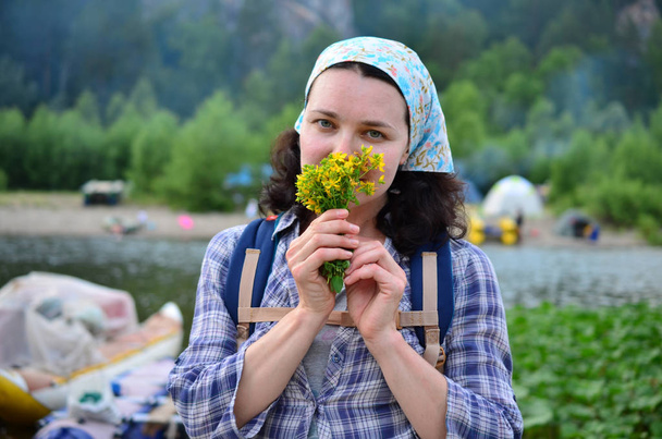 Reizende meisje ruikt gele bloemen ontleend aan de natuur op de achtergrond van de rivier - Foto, afbeelding