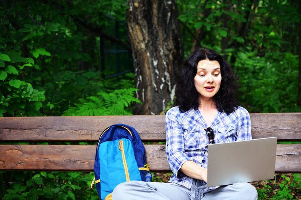 Reisende Frau mit Laptop im Park. Konzept der freiberuflichen Arbeit auf Reisen, die sich mit der Natur beschäftigt - Foto, Bild