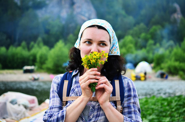 Chica viajera huele flores amarillas tomadas de la naturaleza en el fondo del río
 - Foto, Imagen