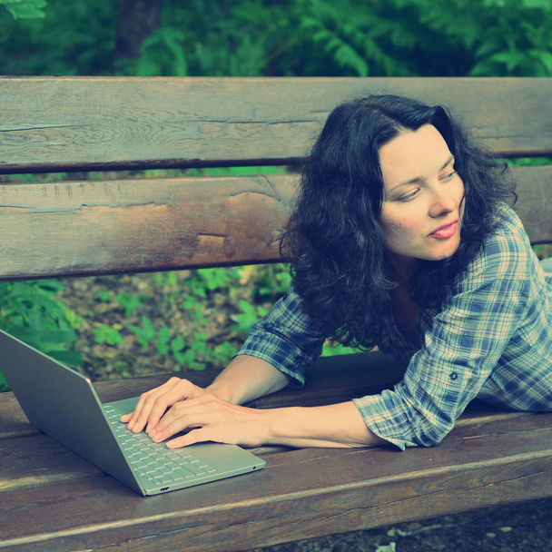 Traveling woman using laptop in park. Concept of freelance work in travelling working on nature - Photo, Image