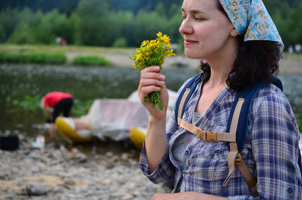 Podróży dziewczyna pachnie żółte kwiaty zaczerpnięte z natury na tle rzeki - Zdjęcie, obraz