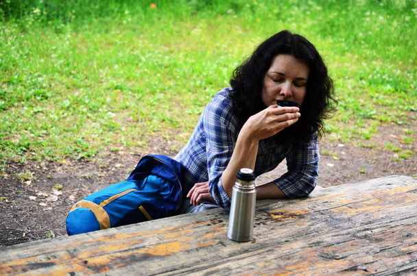 Путешествующая женщина пьет из крышки термоса на открытом воздухе. Девушка отдыхает после прогулки
. - Фото, изображение