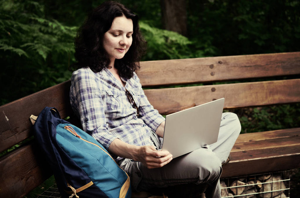 Traveling woman using laptop in park. Concept of freelance work in travelling working on nature - Photo, Image