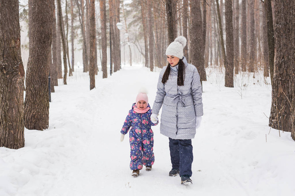 Concept d'hiver, d'enfance et de peuple - maman marche avec sa petite fille dans une forêt enneigée
 - Photo, image