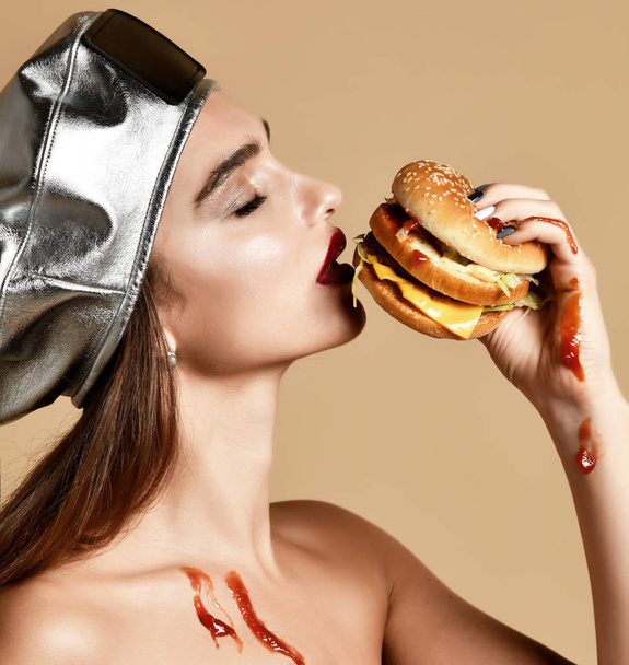 Woman hold burger sandwich  with ketchup with hungry mouth on light brown background - 写真・画像