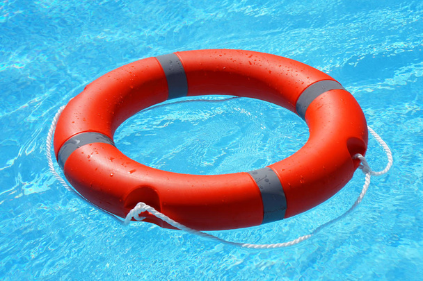 Czerwona koło ratunkowe pływa na niebieskiej wodzie. Pierścień życia unoszący się na słonecznej, niebieskiej wodzie. Pierścień życia w basenie - Zdjęcie, obraz