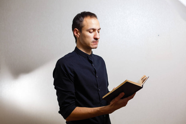 Homem de camisa preta segurando bíblia sagrada no fundo branco
  - Foto, Imagem