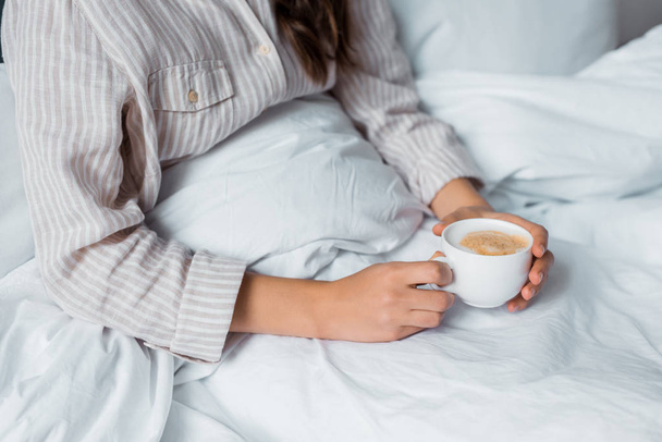 cropped view of woman with cup of cappuccino in bed  - Foto, imagen