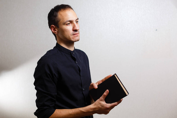 Muž v černé košili držící svatou Bibli na bílém pozadí  - Fotografie, Obrázek