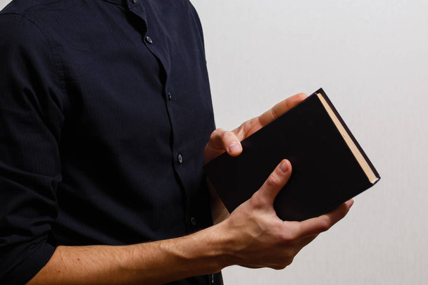 Mies mustassa paidassa pitämässä pyhää Raamattua valkoisella pohjalla
  - Valokuva, kuva