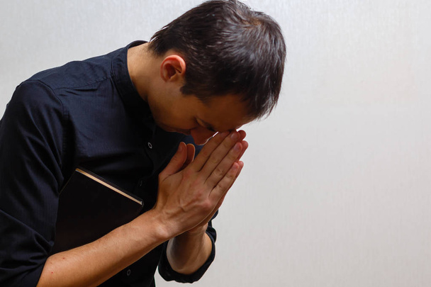 Młody człowiek modli się na szarym tle  - Zdjęcie, obraz
