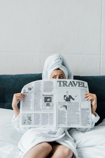 Verwirrtes Mädchen versteckt sich morgens hinter Reisezeitung im Bett   - Foto, Bild