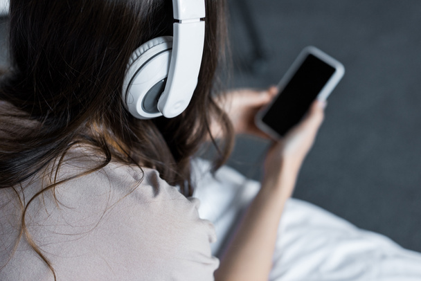 vista recortada de niña escuchando música con auriculares y teléfono inteligente
 - Foto, Imagen