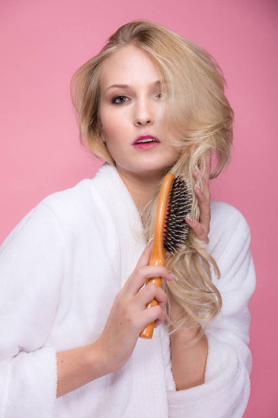jeune femme blonde se brosse les cheveux devant fond rose
 - Photo, image