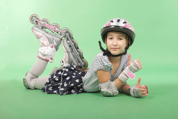 Pretty girl with rollerskates lying on green background - Zdjęcie, obraz
