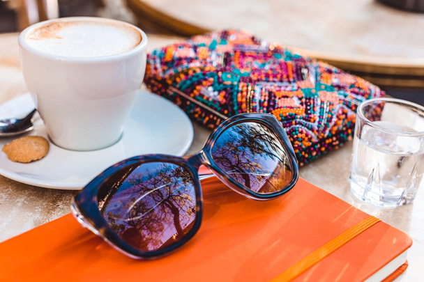 Coffe cappuccino, orange notebook, glass of water and colorful accessories are details of working or studying space, working outside, blogger  - Photo, Image