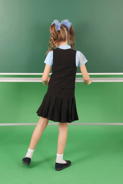 Χαριτωμένο κορίτσι μαθήτρια κοντά σε μαυροπίνακα η έννοια της εκπαίδευσης και της σχολικής ζωής - Φωτογραφία, εικόνα