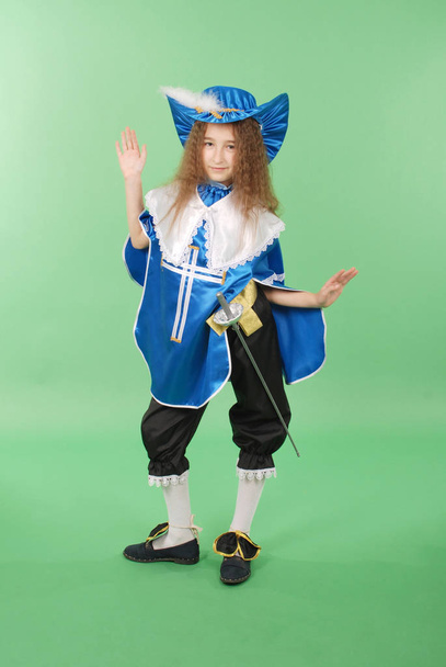 Giovane ragazza come moschettiere in costume blu con bel cappello blu con piume su sfondo verde
 - Foto, immagini
