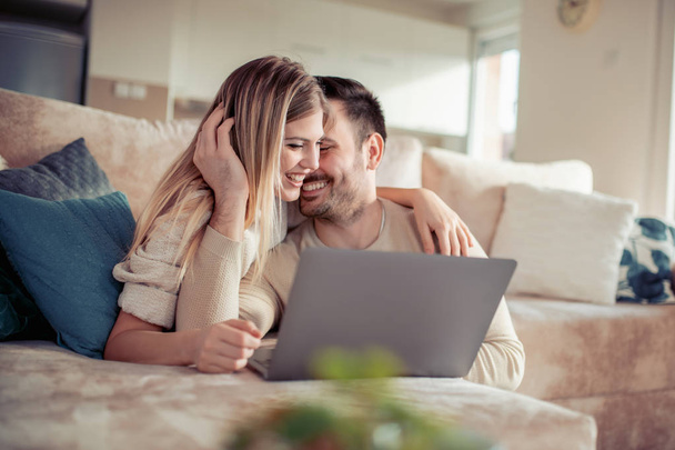 Couple heureux utilisant un ordinateur portable, assis sur un canapé dans le salon à la maison
. - Photo, image