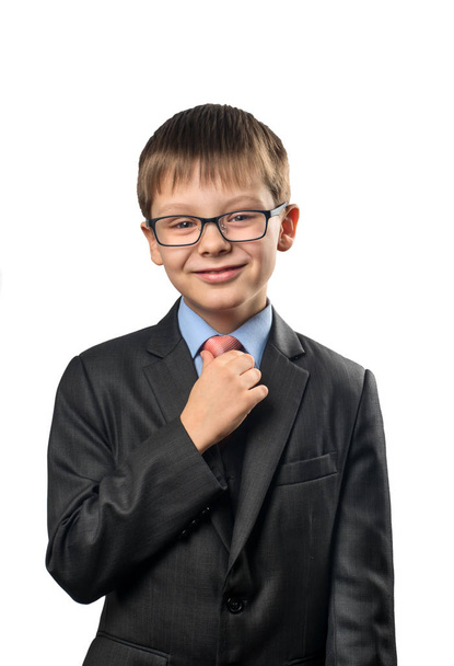 Mosolygó iskolás kiegyenesíti a nyakkendőjét, fehér háttér - Fotó, kép