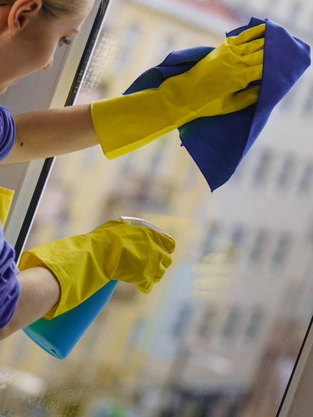 Giovane donna in guanti gialli pulizia vetro della finestra a casa con straccio e detergente spray. Concetto pulizia - Foto, immagini