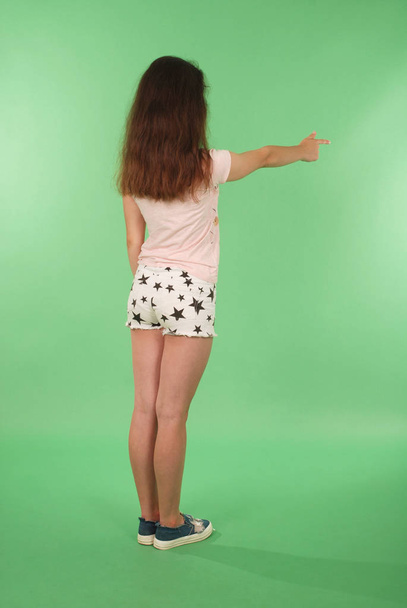 Side view young girl with raised hand looking at wall. Isolated on green background - Photo, Image