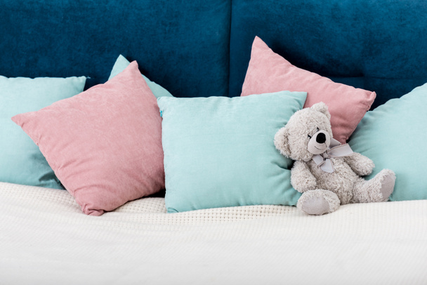 αρκουδάκι τοποθέτηση στο κρεβάτι με τα μαξιλάρια σε φόντο - Φωτογραφία, εικόνα