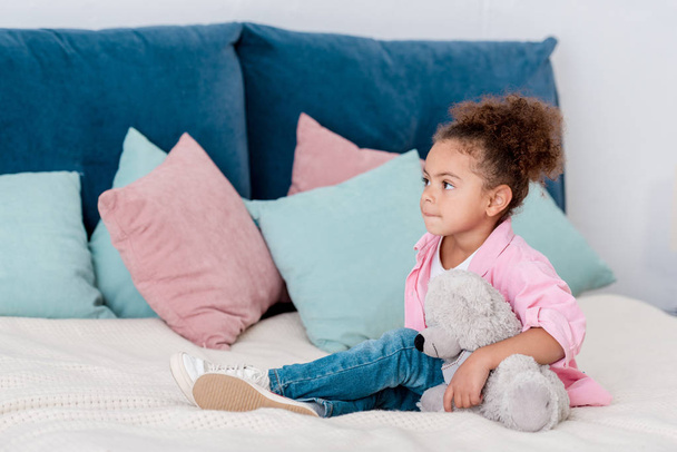 Onu oyuncak ile yatakta çok güzel Afro-Amerikan çocuk seatting   - Fotoğraf, Görsel