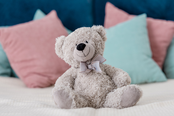 Vista horizontal cercana del oso de peluche sentado en la cama con almohadas en el fondo
 - Foto, Imagen