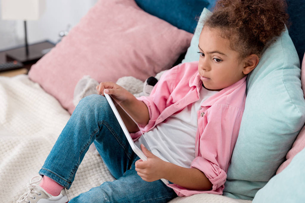 enfant afro-américain réfléchi couché sur le lit avec tablette numérique
 - Photo, image
