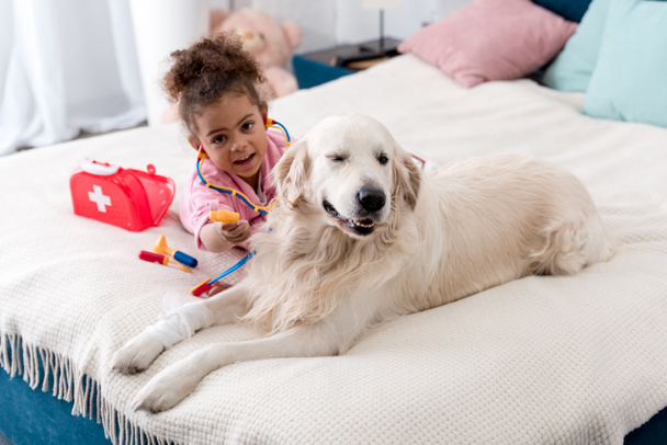 Cute african american child playing with her toys and golden retriever - Foto, Bild