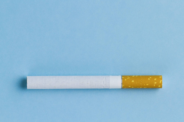 Nicotine, tobacco addiction. Harmful, unhealthy habit. A cigarette lies on a blue background. Smoking concept  - Foto, Imagen