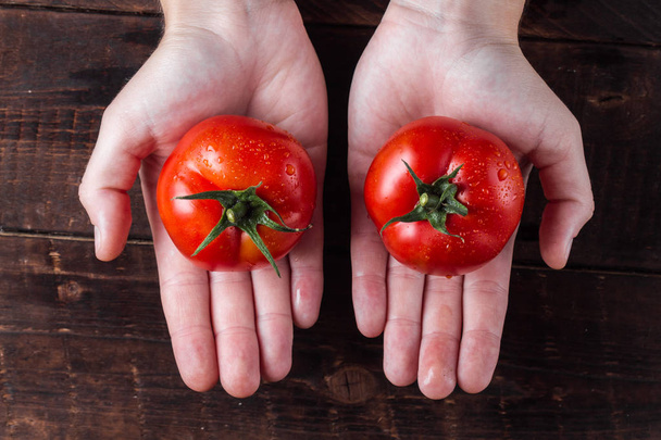 Red, fresh tomatoes in a hands on a dark, wooden background. - Photo, Image