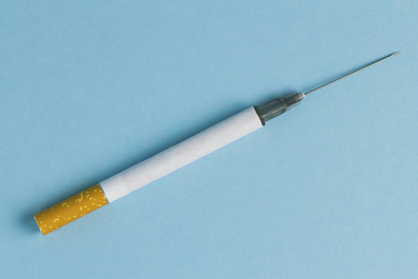 Zigarette und Nadel für Injektionen auf blauem Hintergrund. das Konzept von Tabak, Zigarette, Nikotin, Drogenabhängigkeit. Gesundheitsschäden. Konzept Rauchstopp - Foto, Bild