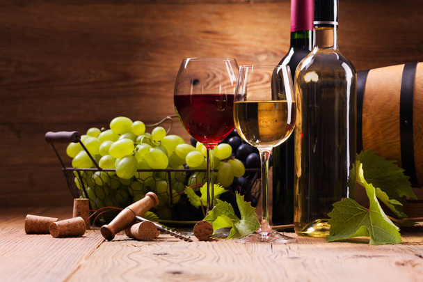 Glasses of red and white wine, served with grapes on a wooden background - Фото, изображение