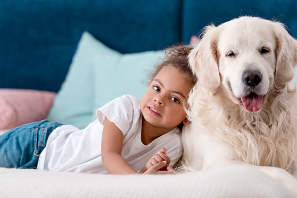 Adorable little african american kid with happy dog lying on bed - Foto, immagini
