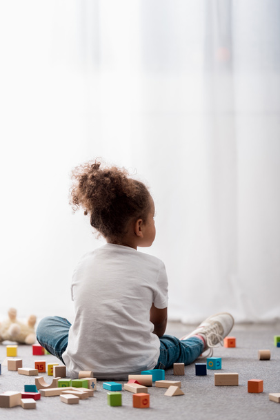 Вид ззаду маленької дитини в білих футболках в оточенні барвистих іграшкових кубиків
 - Фото, зображення