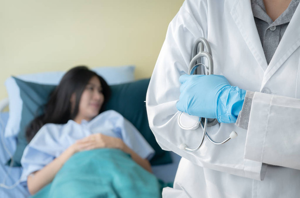 Close-up van de hand van dokter stethoscoop bedrijf en staande op de zachte blured van de patiënt vaststelling op bed in het ziekenhuis - Foto, afbeelding