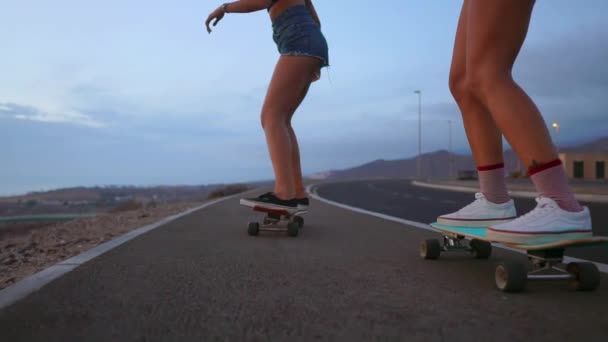 Dvě dívky skateboardista projížďky na vývěsku na svahu proti obloze z hory. Zpomalený pohyb steadicam - Záběry, video