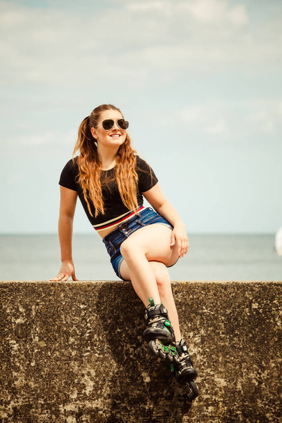 Happy joyful young woman wearing roller skates relaxing after long ride. Female being sporty having fun during summer time near sea. - Photo, image
