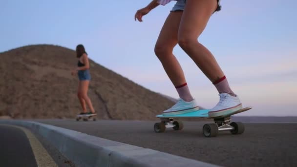 Dvě dívky skateboardista projížďky na vývěsku na svahu proti obloze z hory. Zpomalený pohyb steadicam - Záběry, video