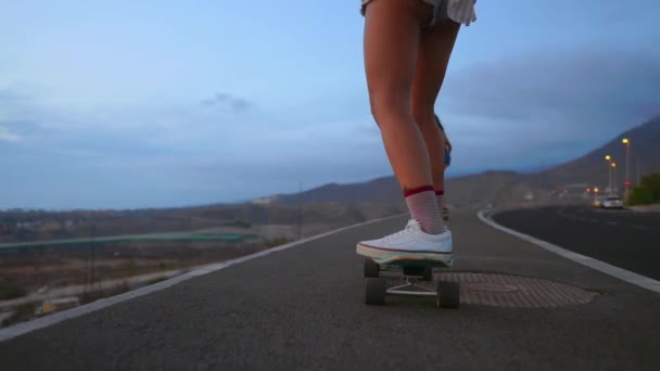 Skateboardista žena jezdí na tabuli na svahu proti obloze z hory - Záběry, video